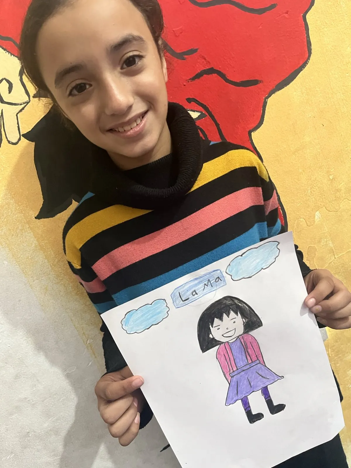 Young girl holding up her drawing of a character named Lama at the workshop